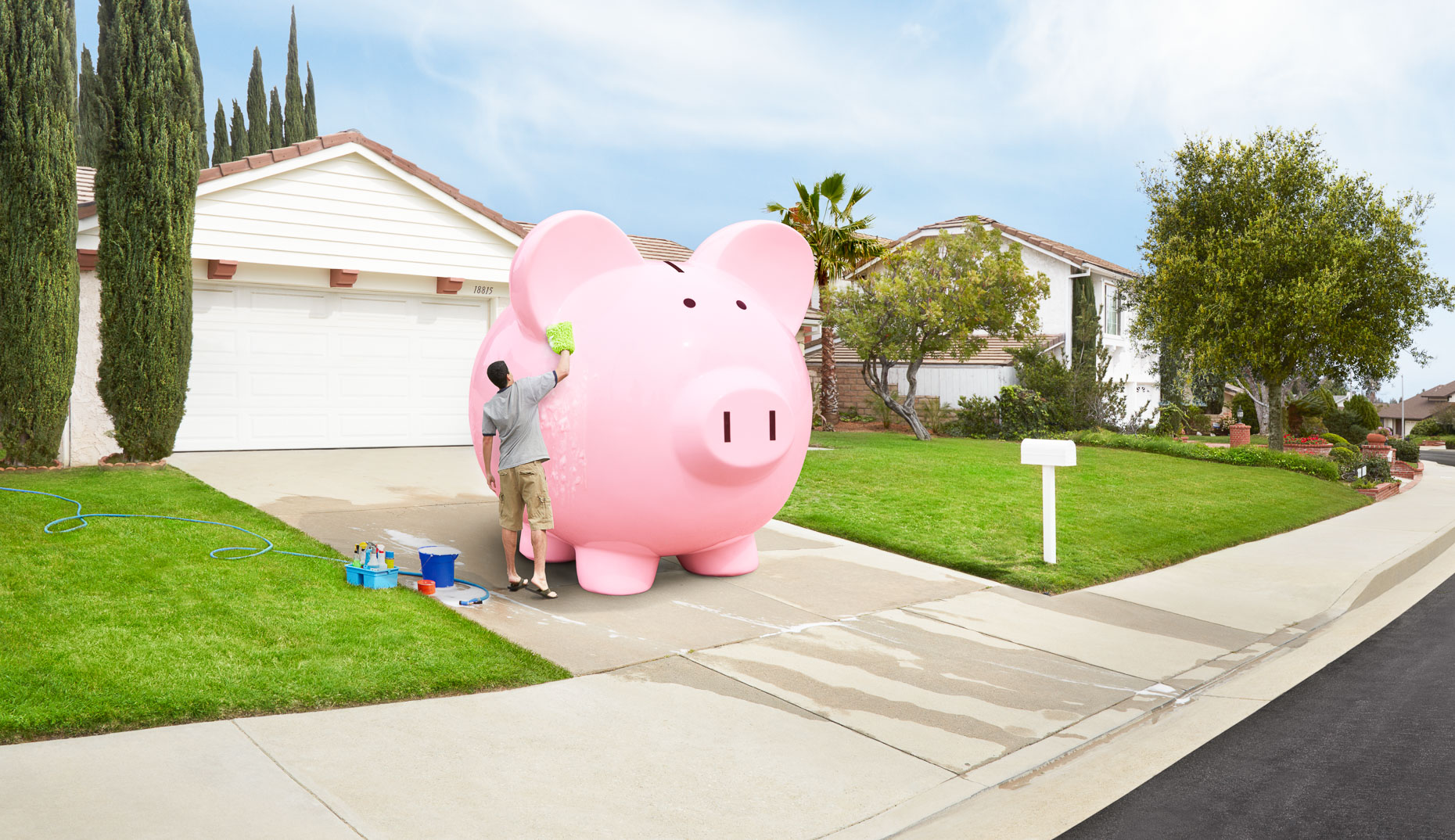 Man washing huge pink piggy bank in driveway of house. David Zaitz.