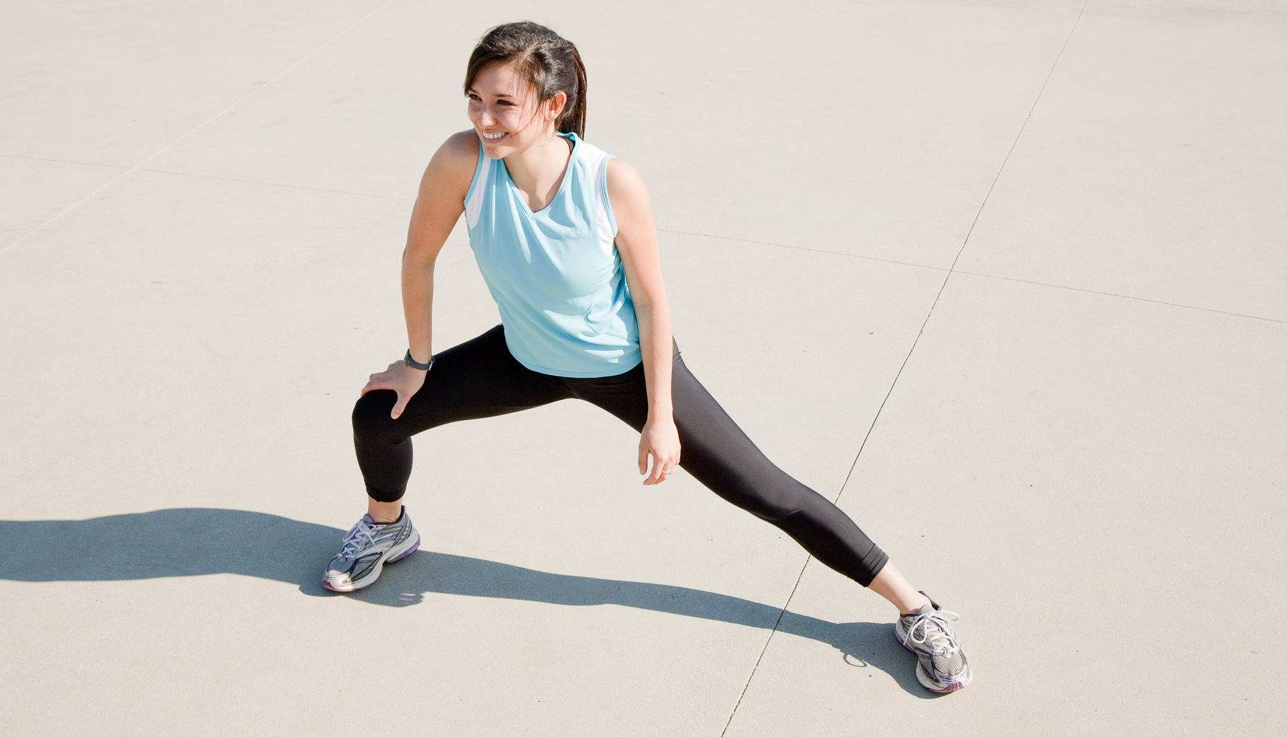 Smiling woman stretching for workout in running clothes against concrete sidewalk background by David Zaitz Photography.