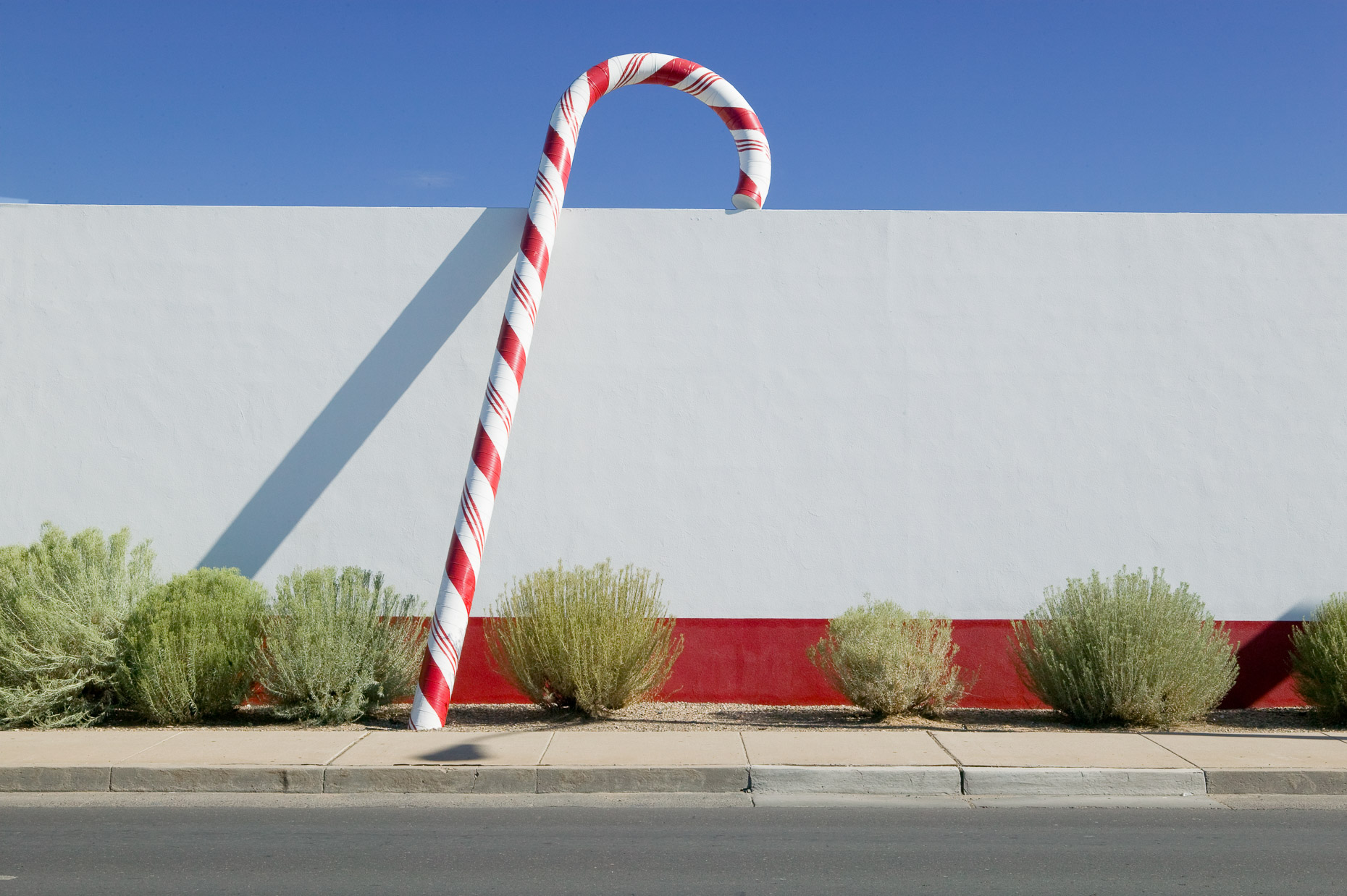 Large candy cane prop against white wall of commercial building by David Zaitz