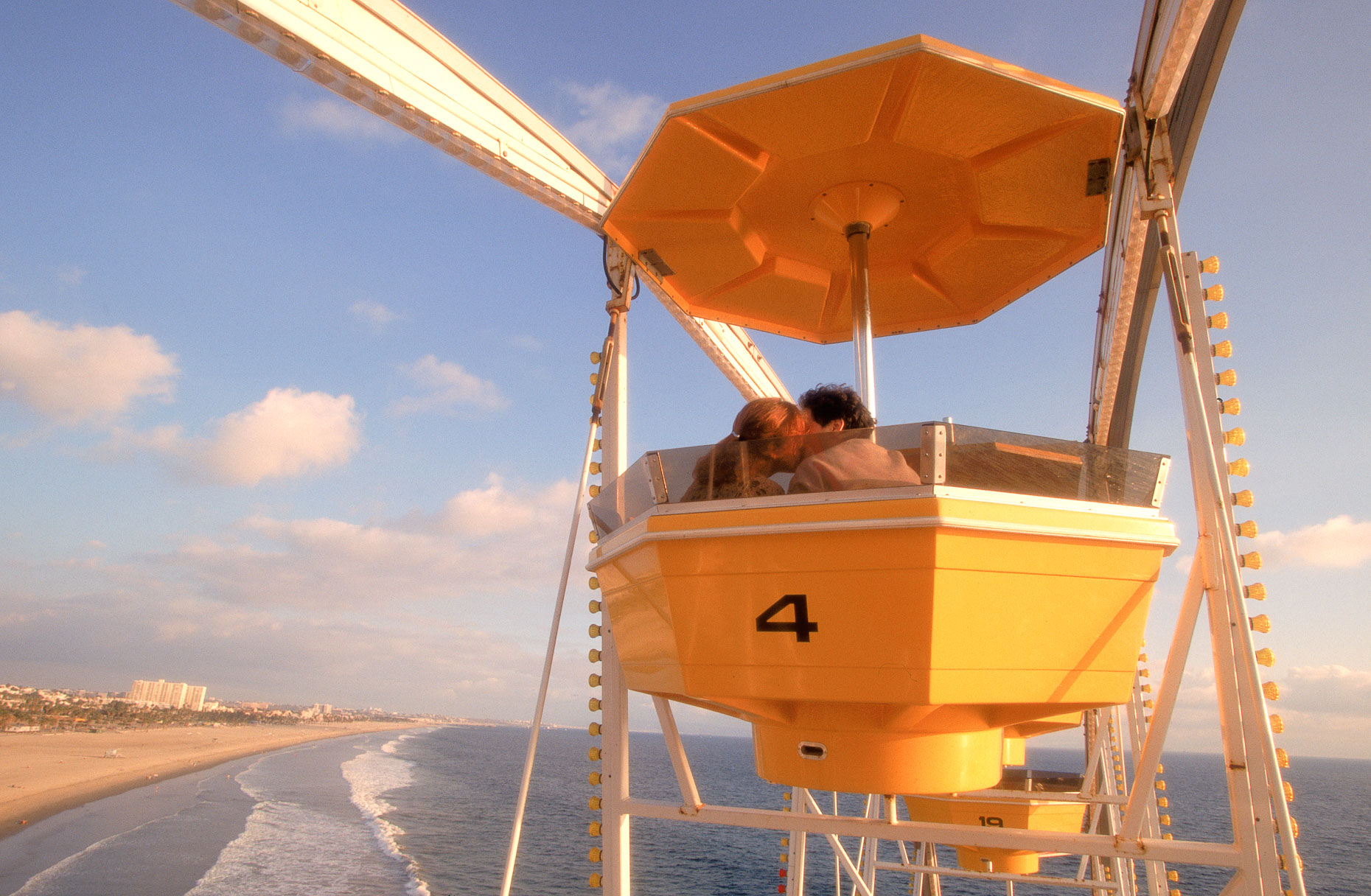 Couple in Ferris wheel car kissing with beach shore in background in Santa Monica, California