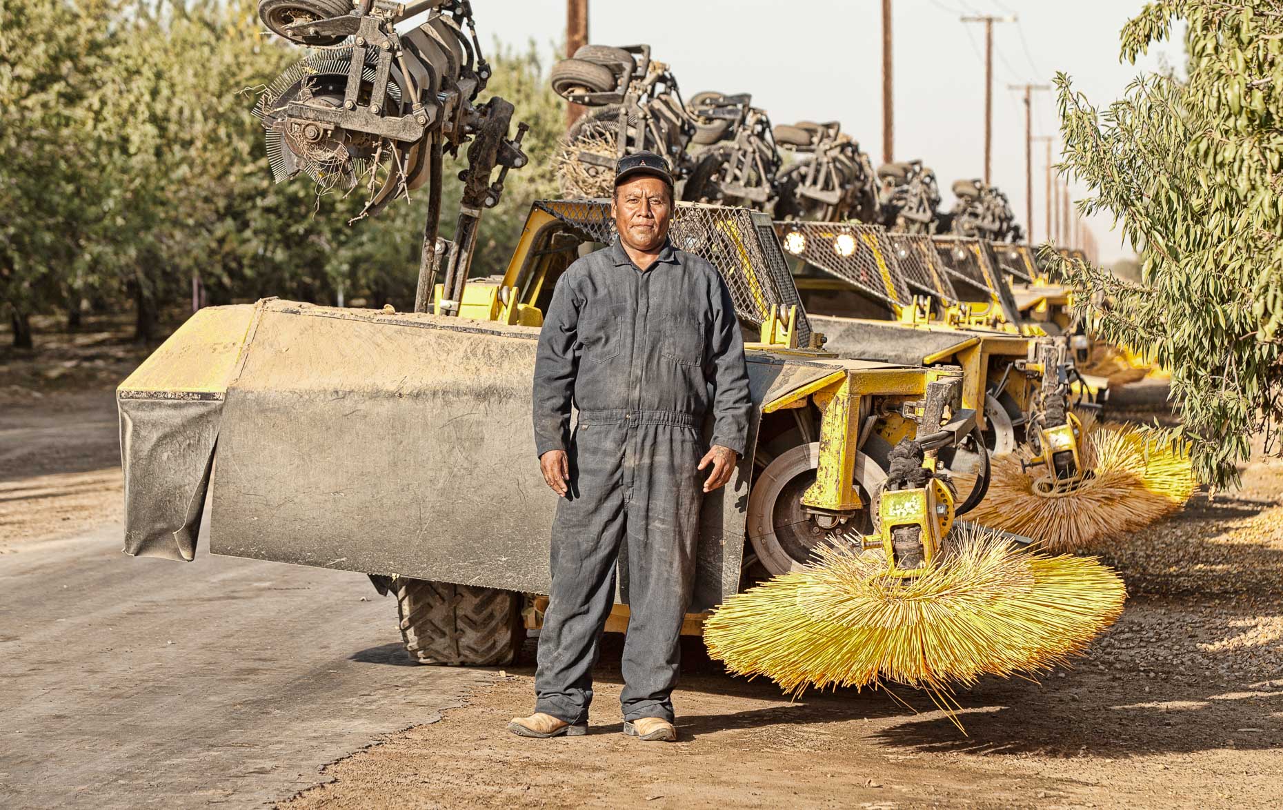 Portrait of farm orchard worker standing in front of sweeper machine in almond orchard near Lost Hills, California by David Zaitz