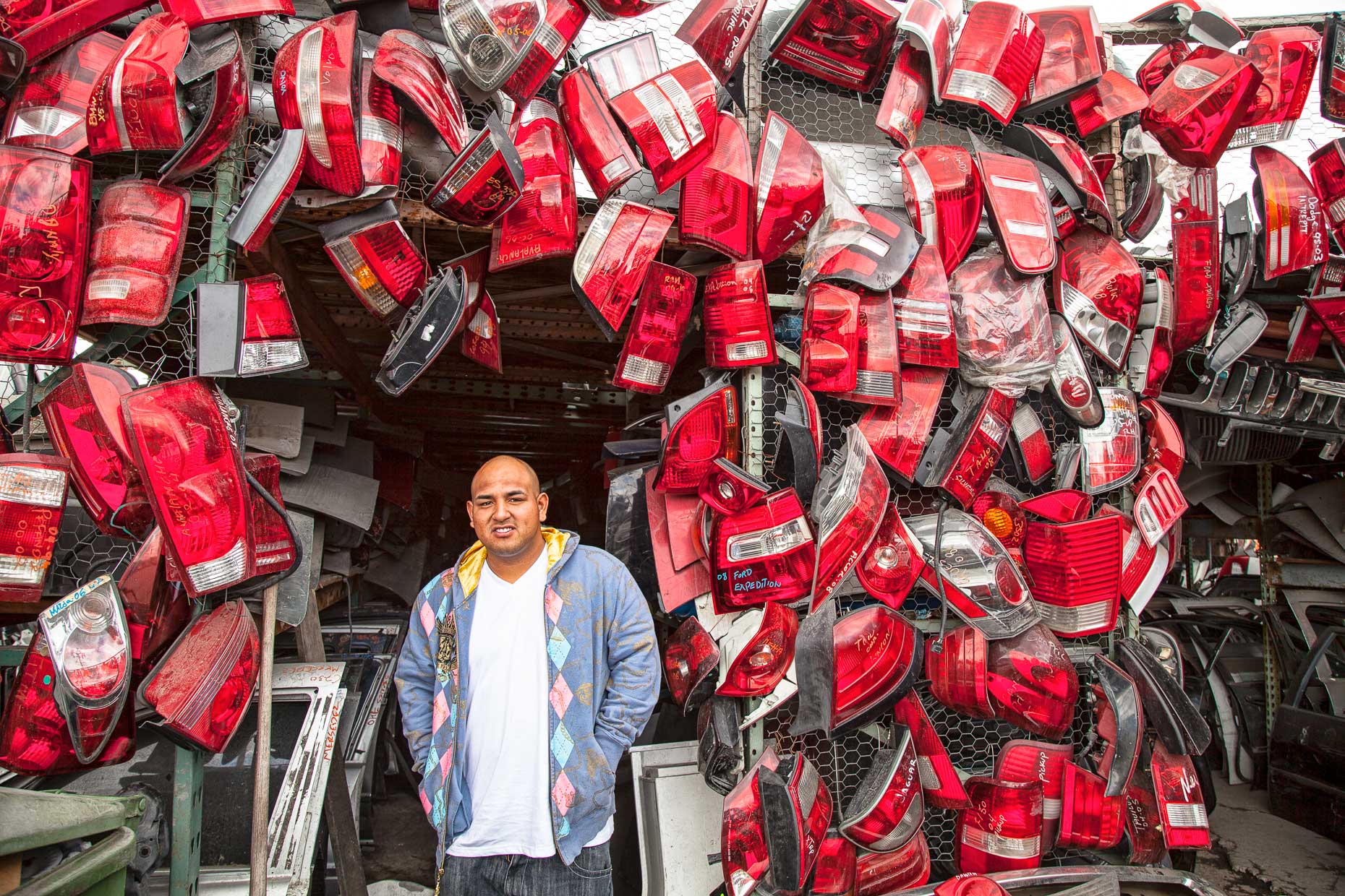 Portrait of man standing by display of used automotive tail light assemblies by David Zaitz