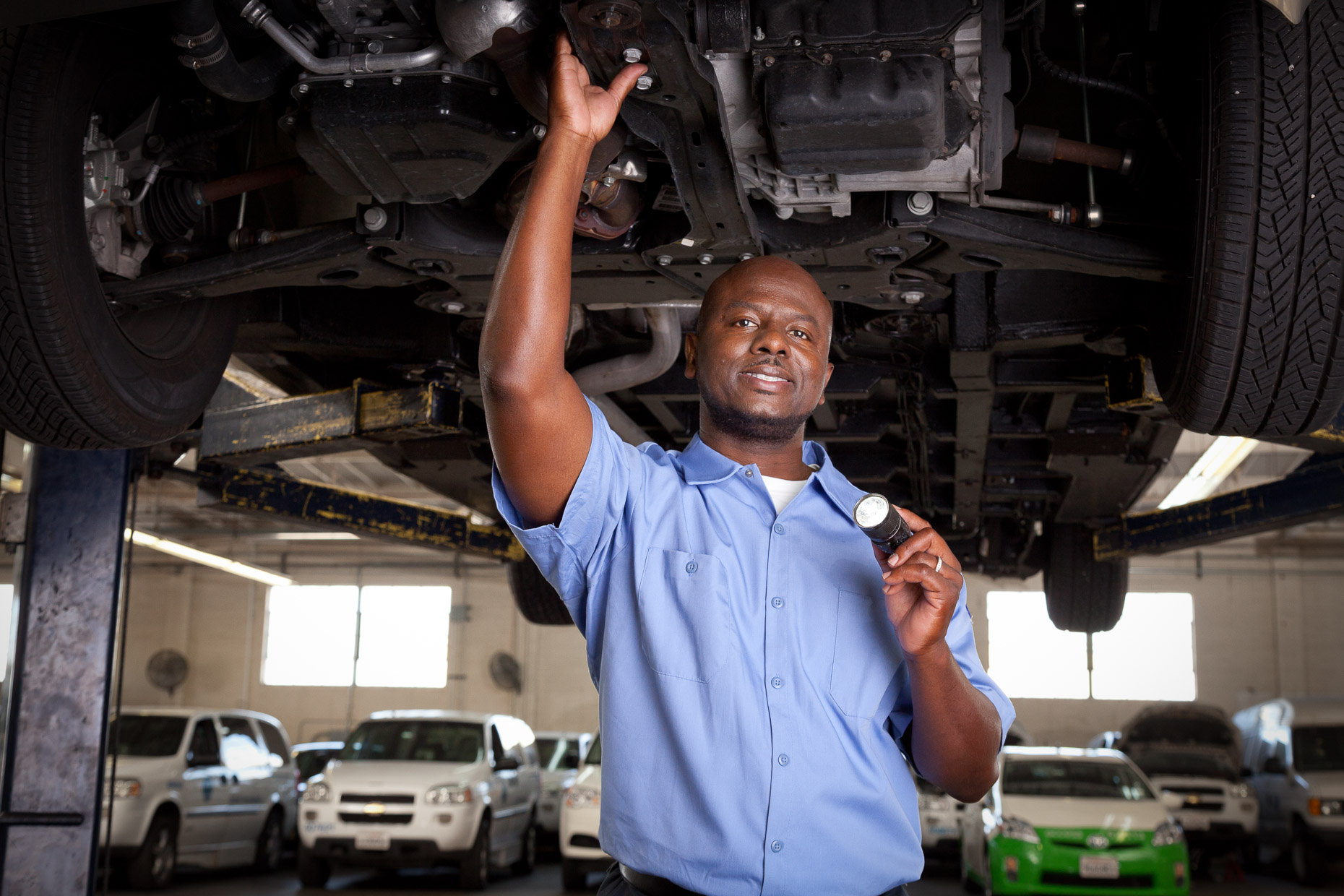 Portrait of automotive mechanic repairman inspecting underside of vehicle in repair garage by David Zaitz