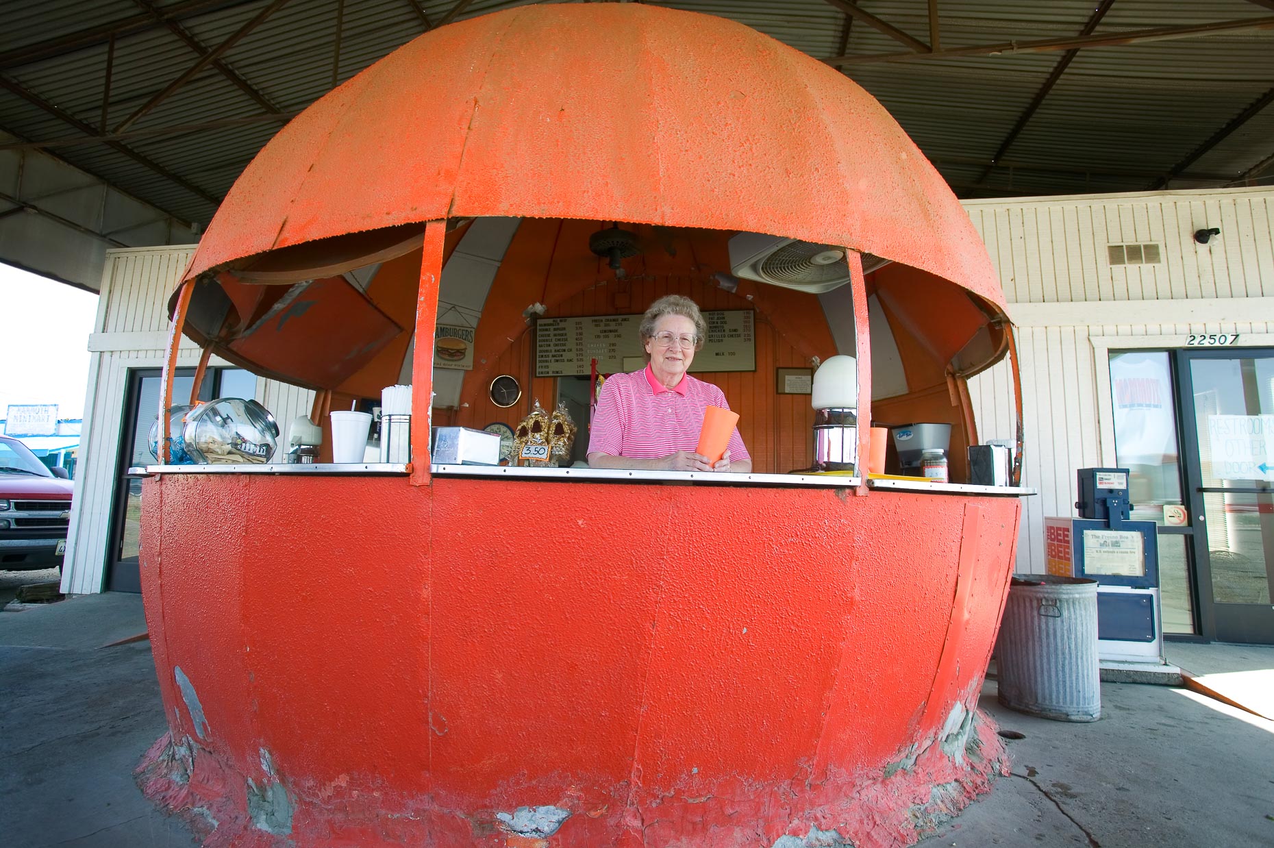 Portrait of woman standing in orange shaped roadside juice stand in Madera, California by David Zaitz