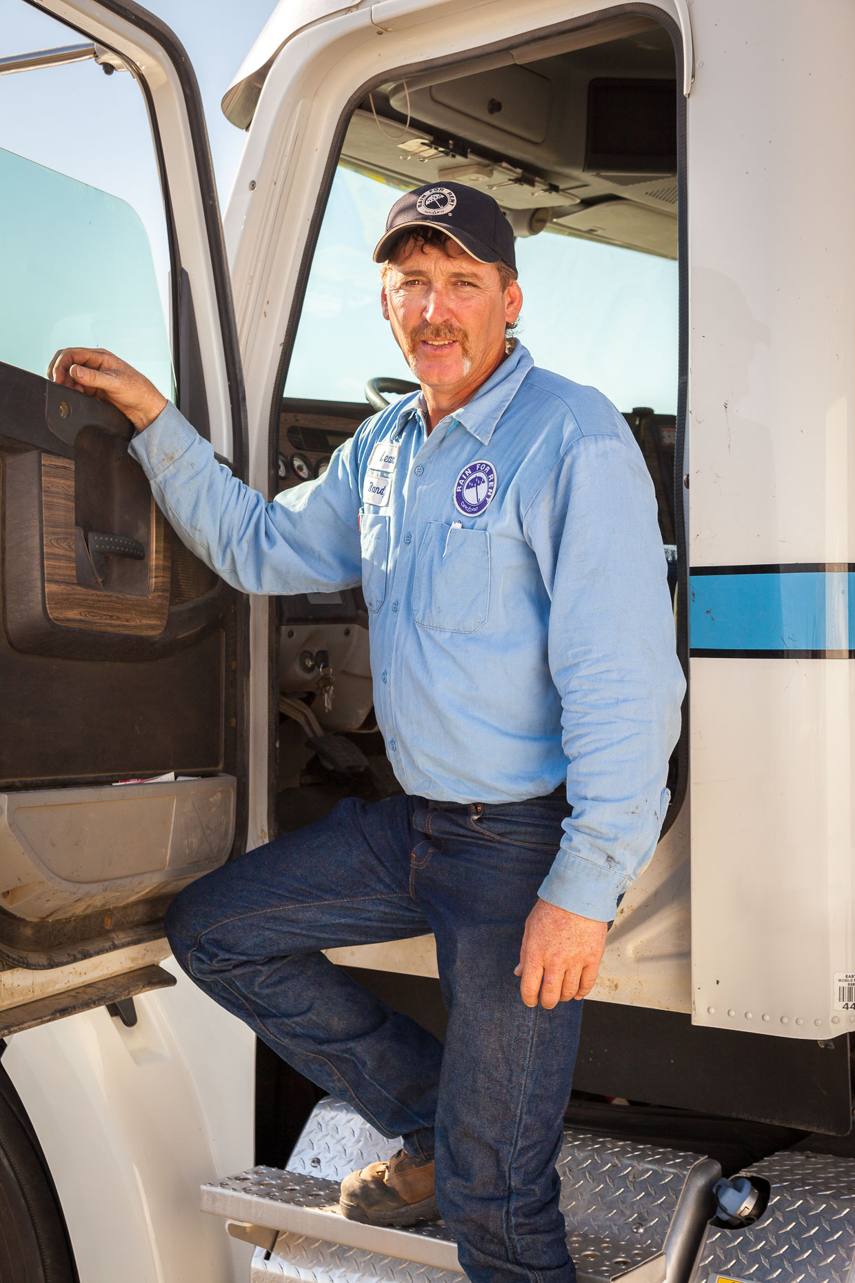 Environmental portrait of truck driver standing in open truck cab by David Zaitz