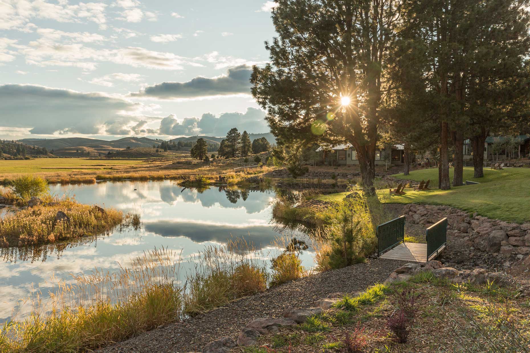 Sunset over pond at Silvies Valley Ranch with bridge, lawn chairs, trees, David Zaitz