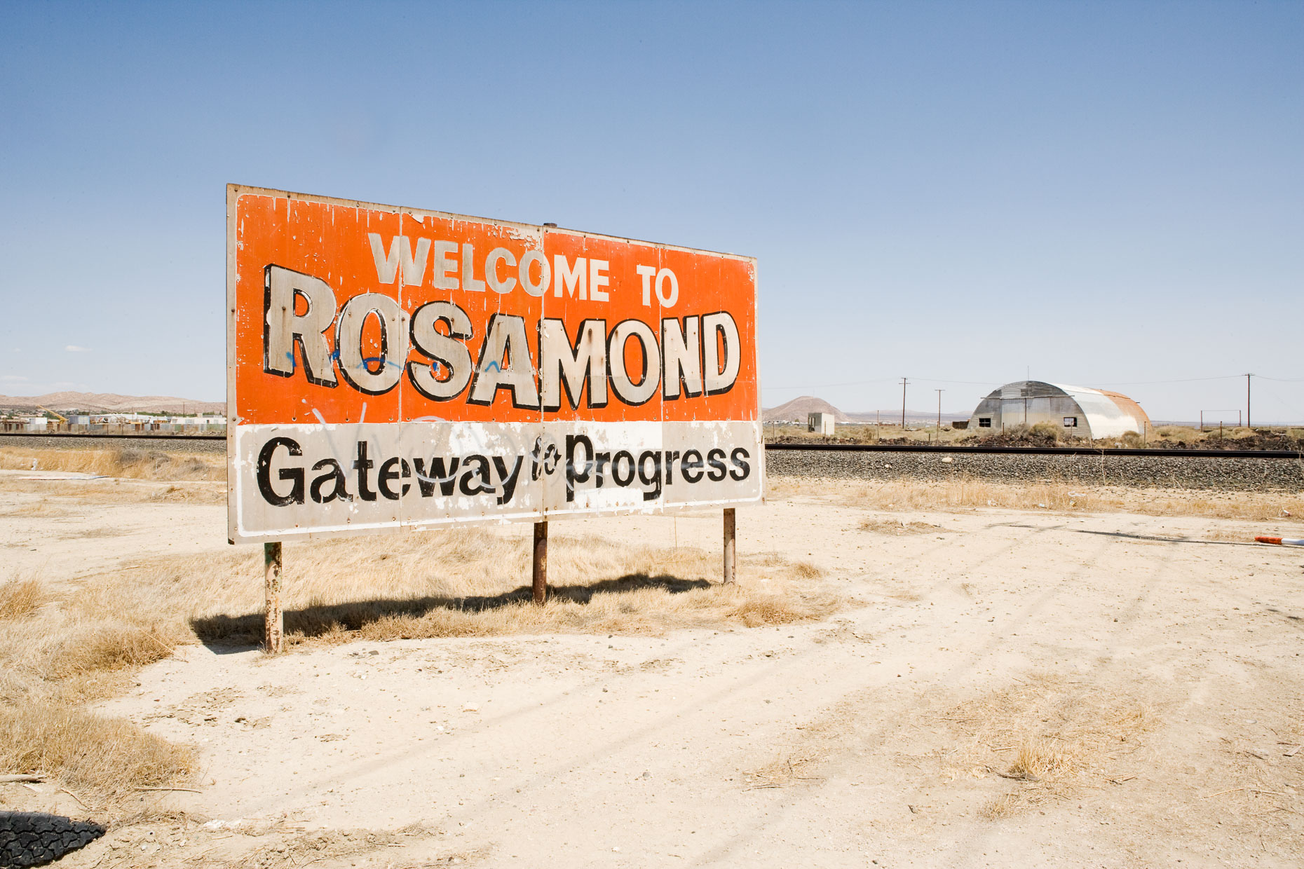 Weathered WELCOME TO ROSAMOND GATEWAY TO PROGRESS billboard on road in desert. Rosamond, California by David Zaitz