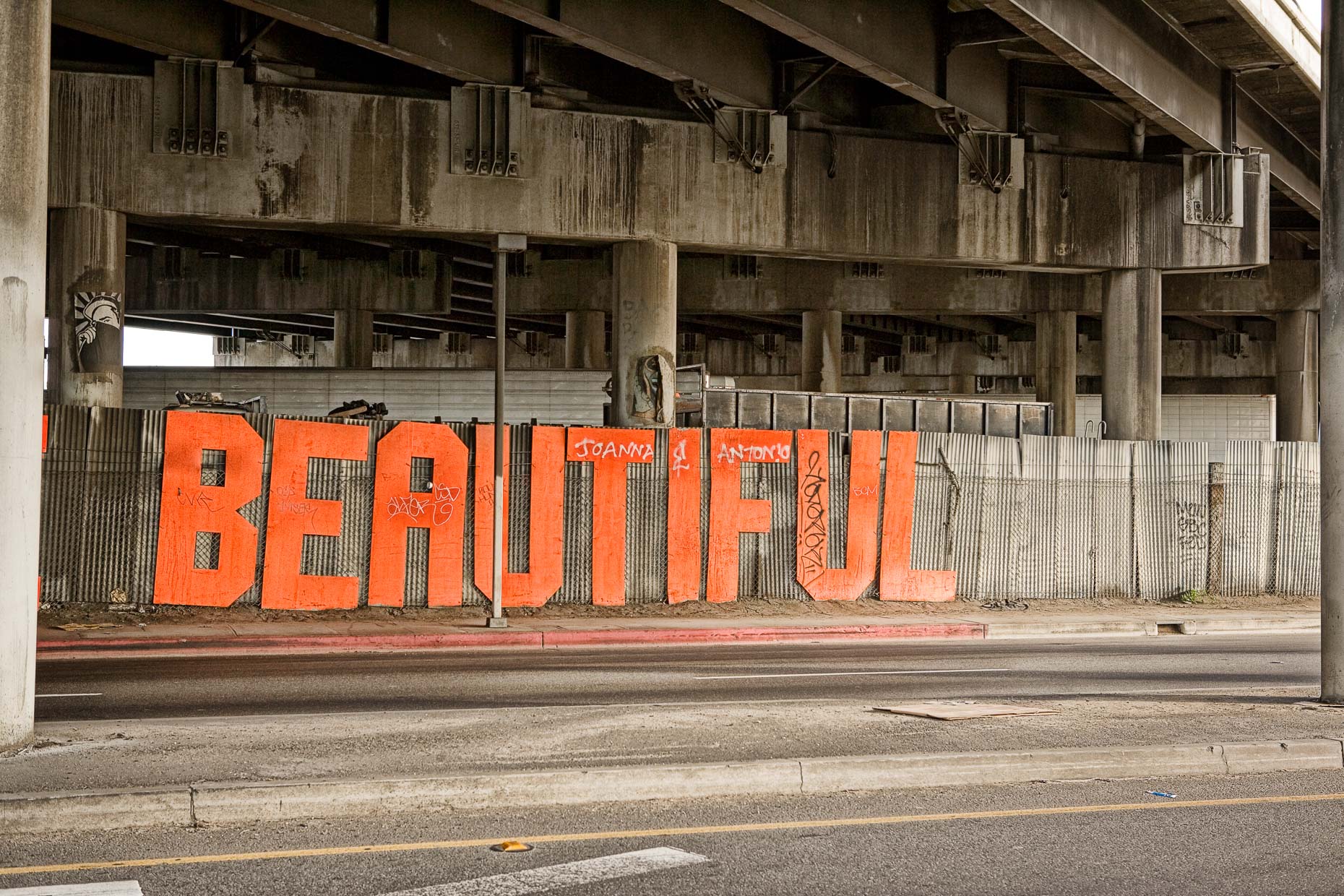 YOU ARE BEAUTIFUL sign is dirty, hanging on fence under freeway overpass in Los Angeles, California by David Zaitz