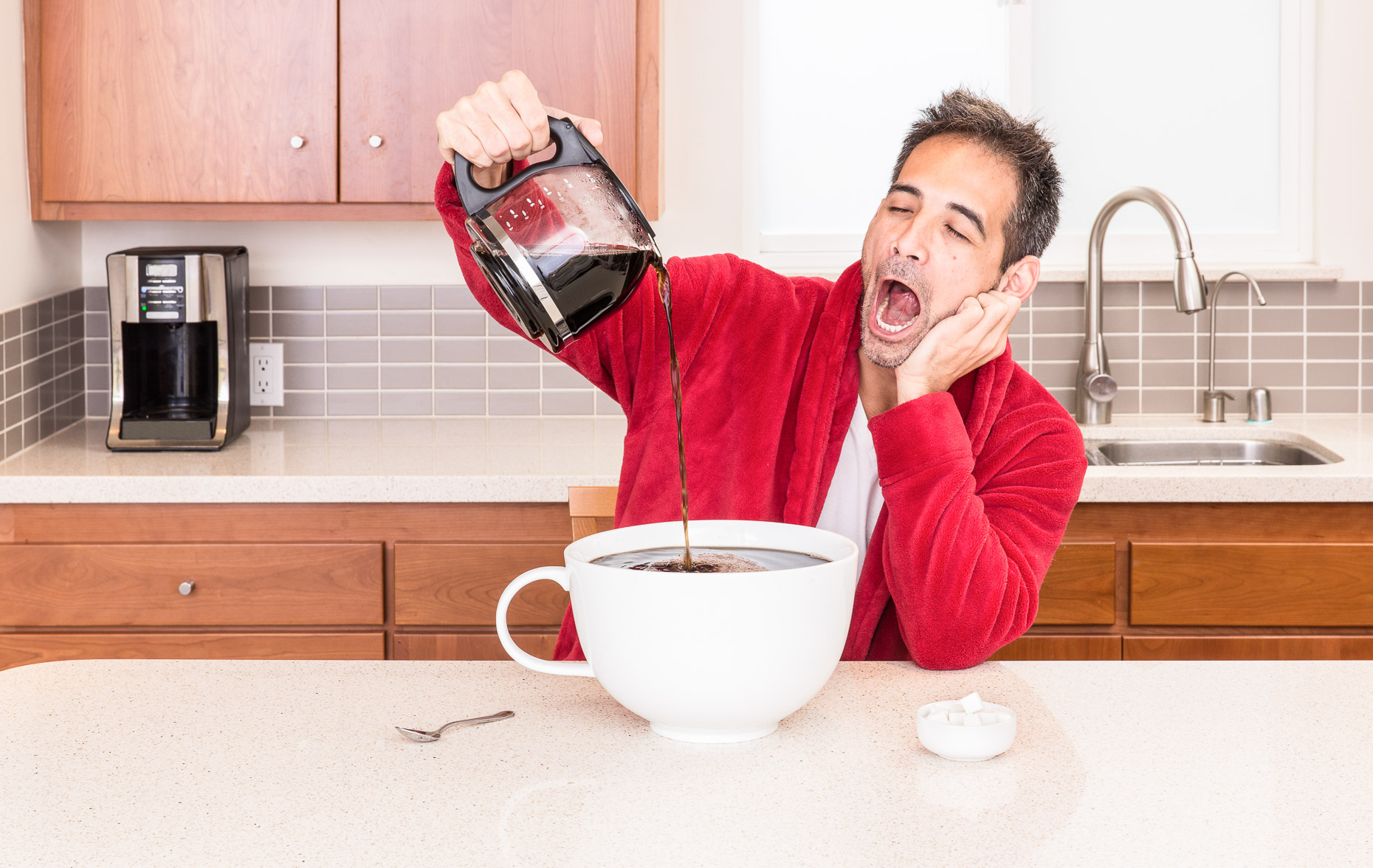 Sleepy tired man yawning in robe in kitchen pouring huge large cup of coffee. David Zaitz.