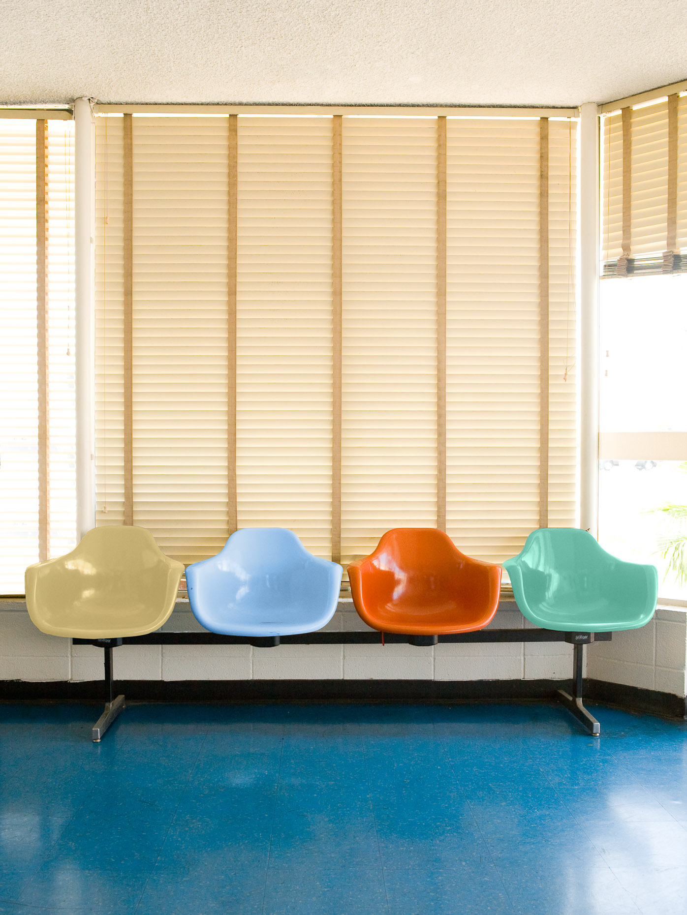 Moulded plastic chairs in a row creating seating in a bus station waiting room with Venetian blinds by David Zaitz 