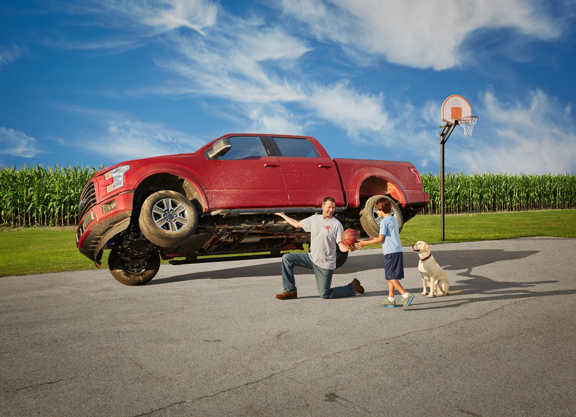 Man lifts up pickup truck to retrieve basketball for boy with dog. David Zaitz.