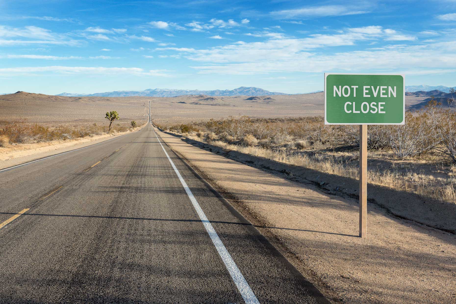 Road on desert highway reads NOT EVEN CLOSE. David Zaitz.