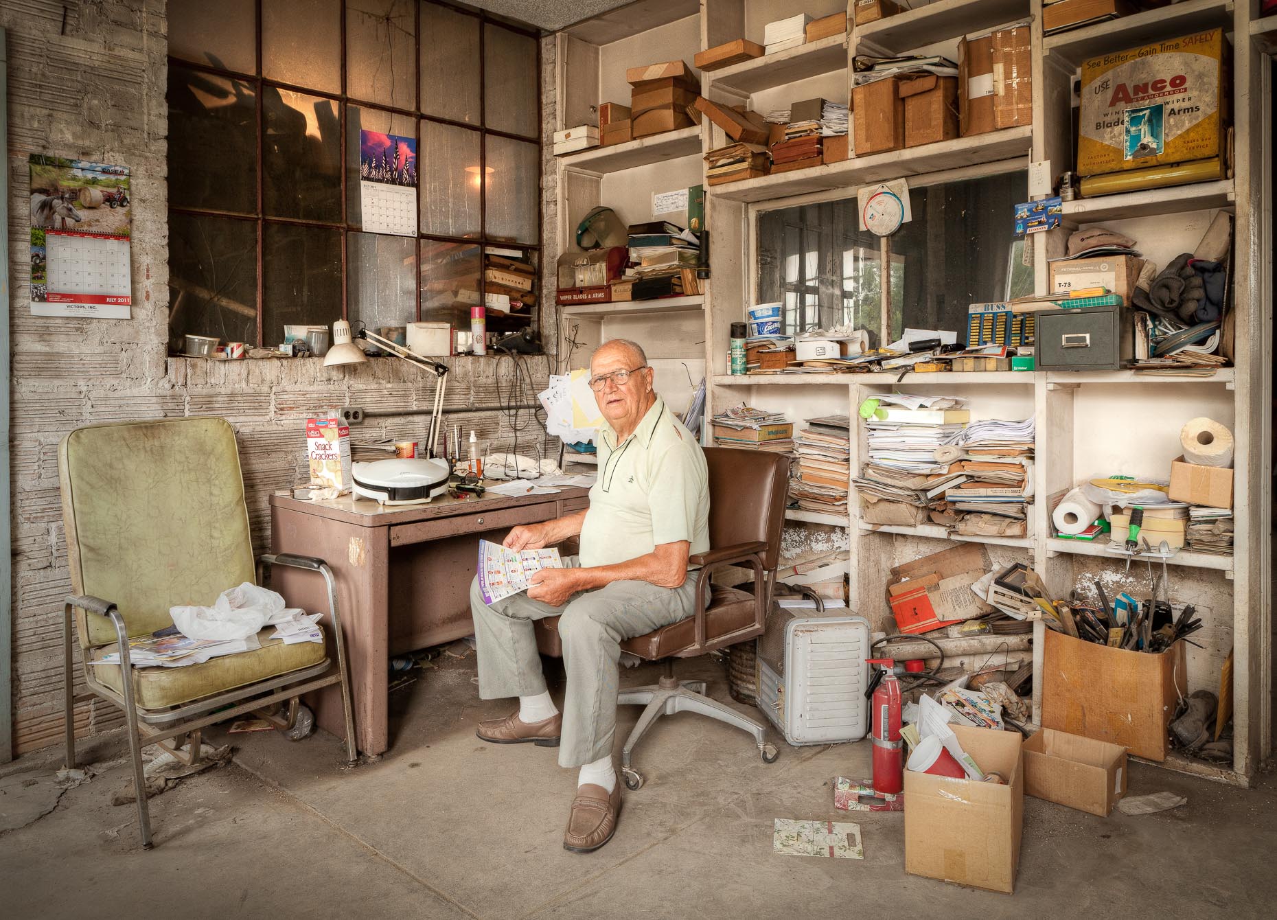 Man sitting in cluttered office of repair garage by David Zaitz