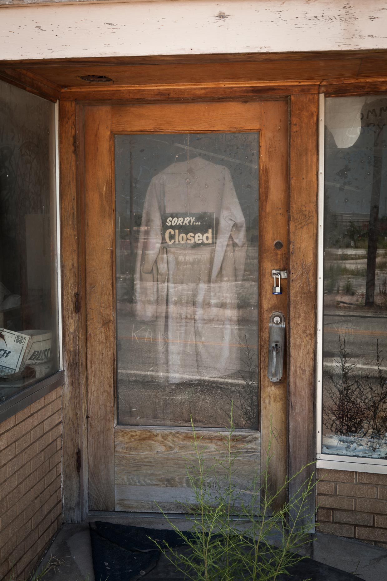 SORRY CLOSED sign in window of store door with clothing hanging by David Zaitz.