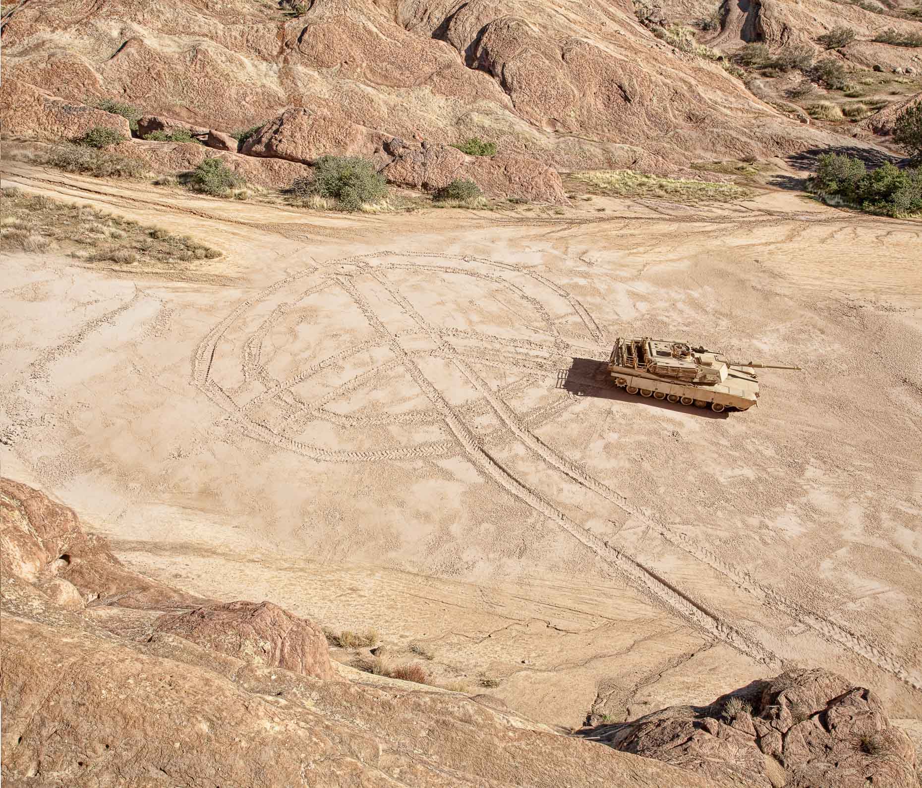 Military tank draws a peace symbol in dirt ground. David Zaitz.