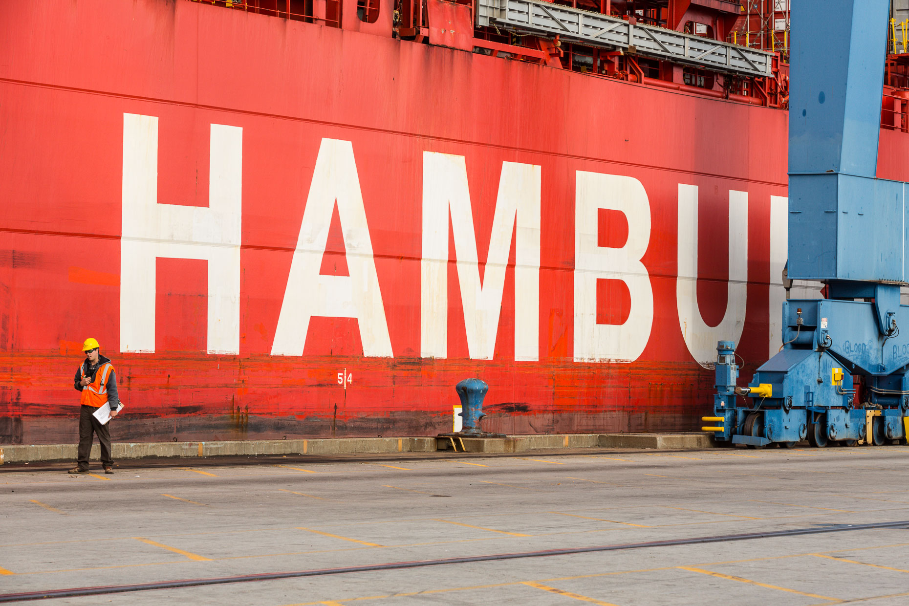 Shipyard working walking past red cargo ship with letters HAMBU in Mt. Pleasant, South Carolina by David Zaitz.