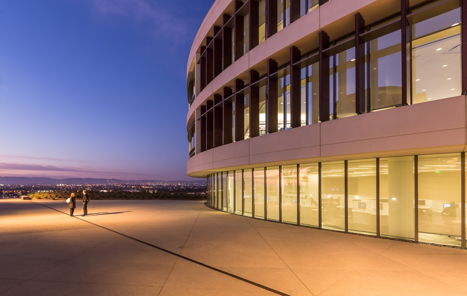 Architecture shot including people standing next to circular building at dusk. Hannon Library at Loyola Marymount University LMU in Los Angeles, California.  David Zaitz Photography.
