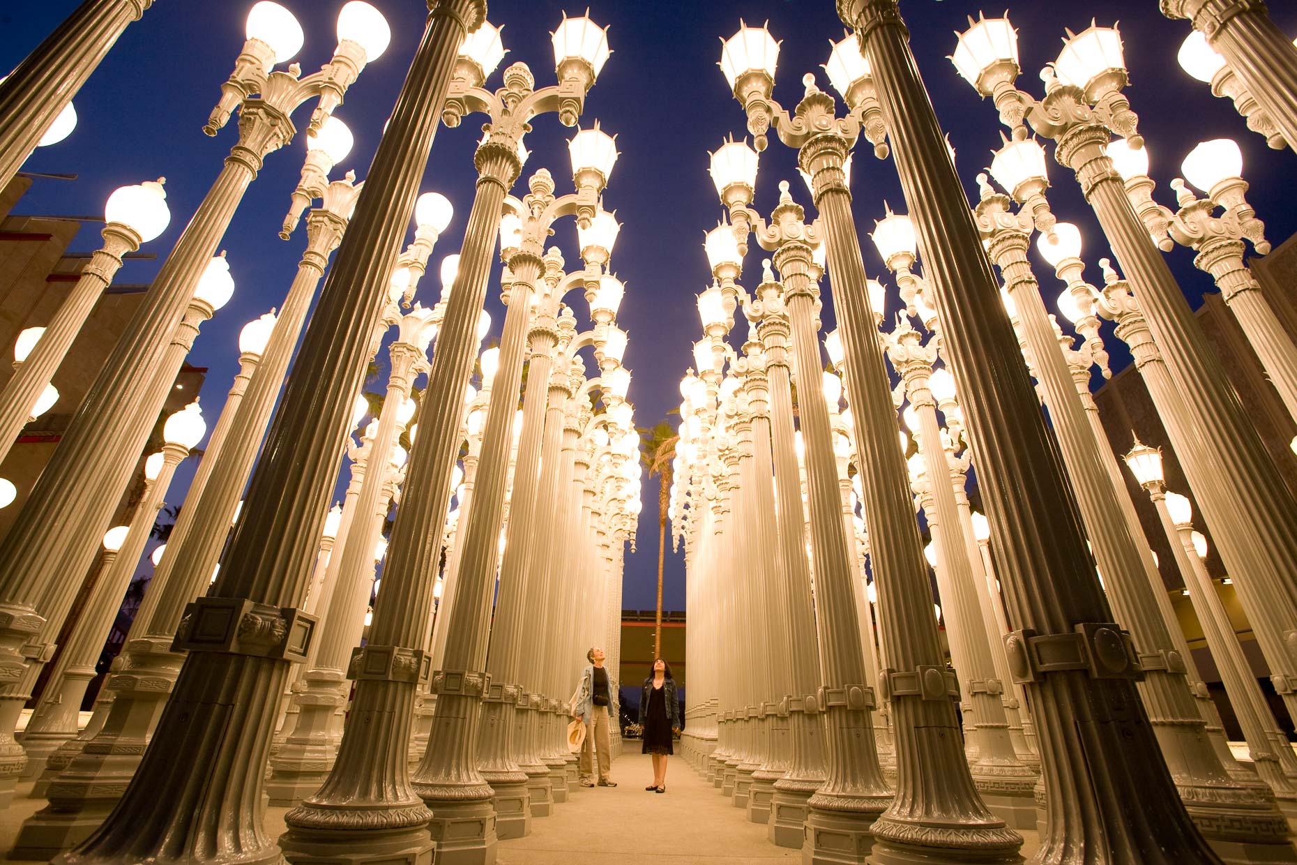 Women standing under array of street lights, an art piece called "Urban Light" by artist Chris Burden at LACMA Los Angeles County Musuem of Art.  David Zaitz Photography.