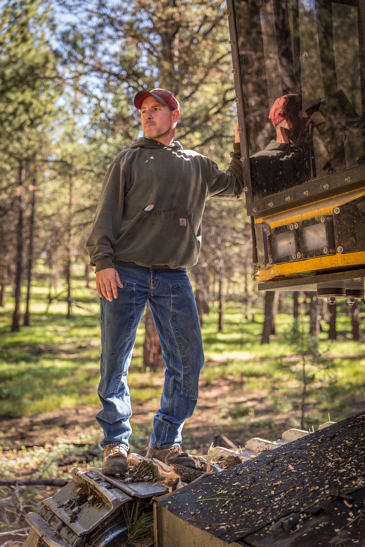 Environmental portrait of man working logging operation in Oregon standing on tree cutting machine, by David Zaitz