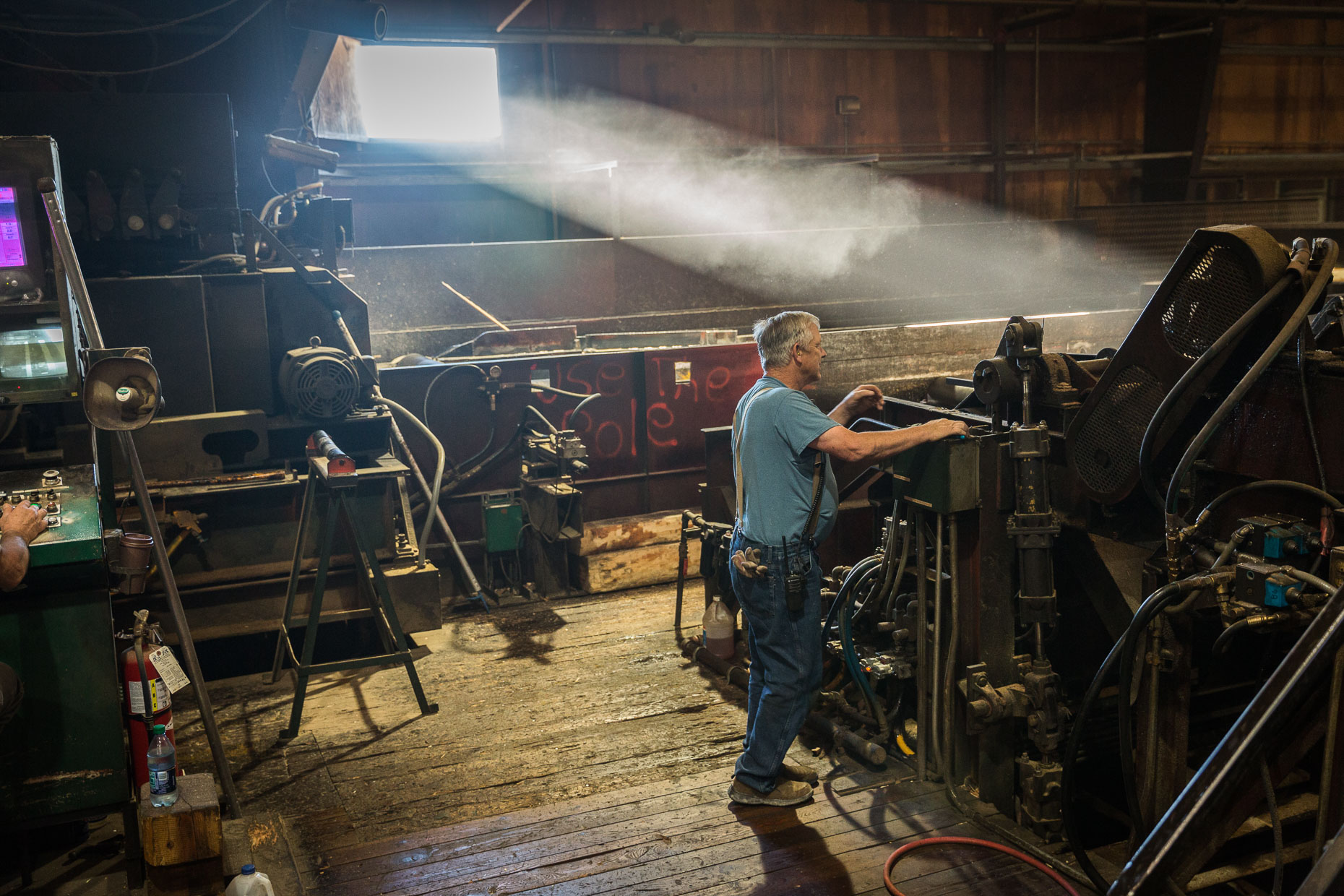 Man worker in lumber mill tends to machinery with shaft of light coming through window, Malheur Lumber Company mill in John Day, Oregon by David Zaitz.