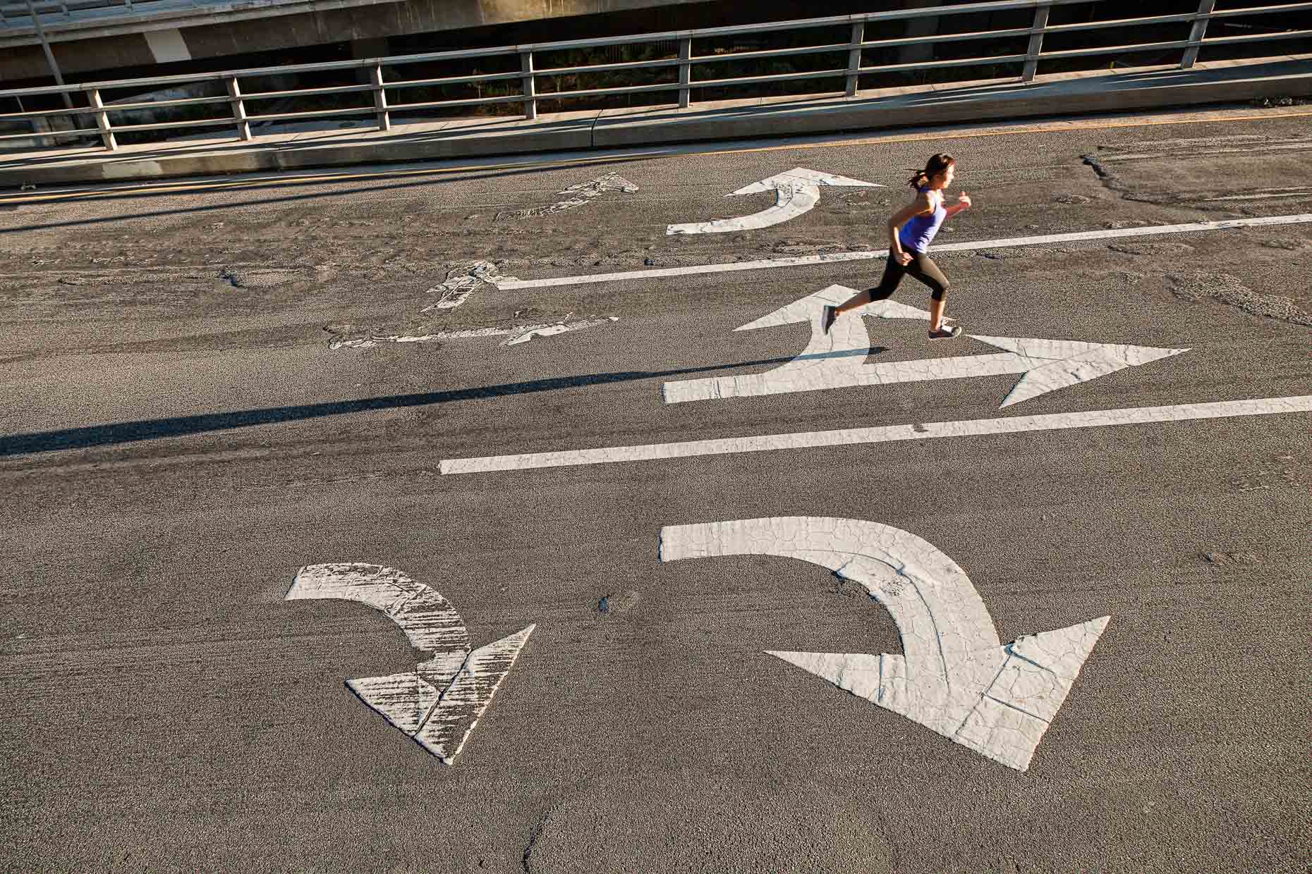 Woman running on city street with arrows in Los Angeles, California by David Zaitz