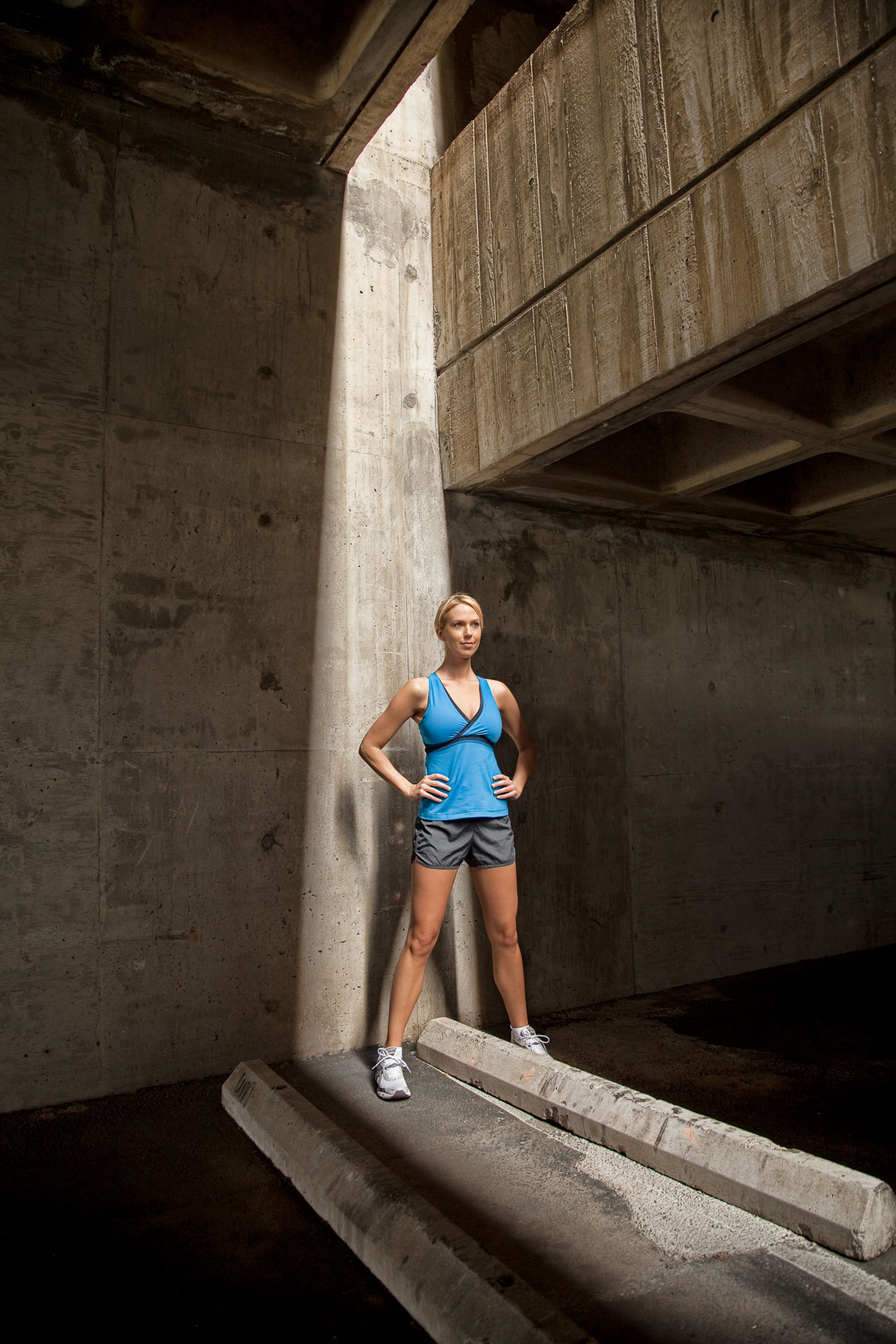Woman in running clothing resting in shaft of light in parking garage by David Zaitz