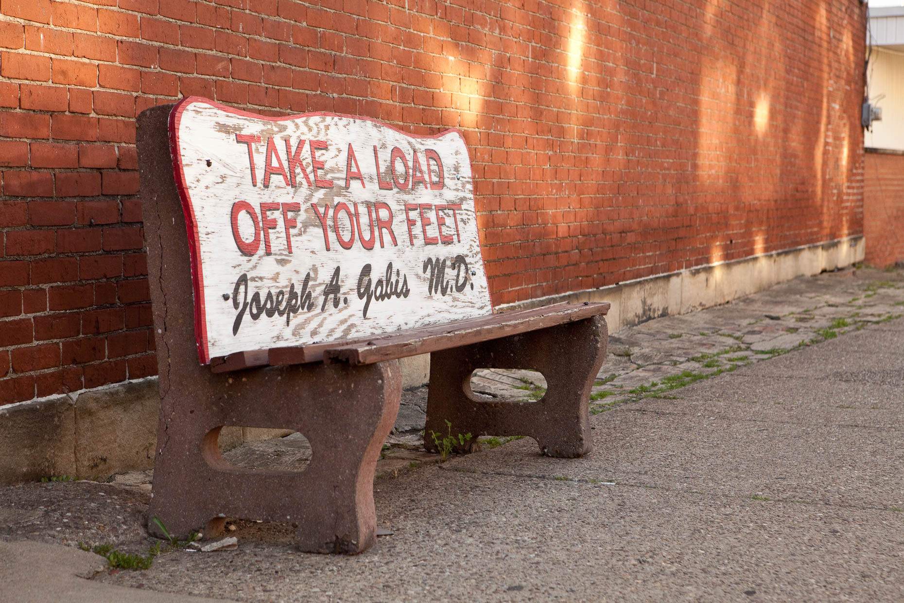 Bus bench with TAKE A LOAD OFF YOUR FEET signage by David Zaitz