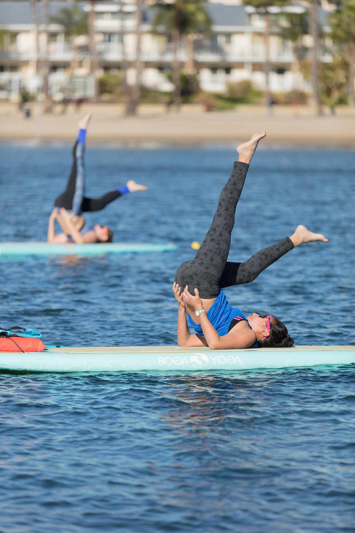 Women practicing yoga will on stand up paddle boards on water in Marina del Rey, California